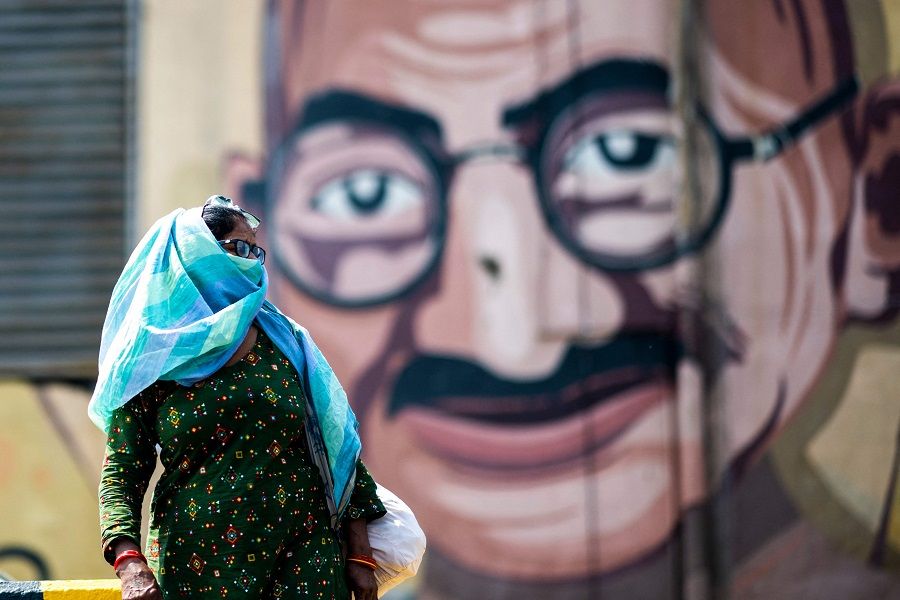 A woman crossing a street passes by a wall art depicting Indian independence hero Mahatma Gandhi during a government-imposed lockdown to prevent the Covid-19 coronavirus from spreading in Noida, India on 21 May 2021. (Jewel Samad/AFP)
