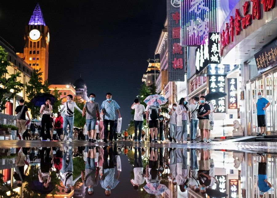 People are reflected in a puddle after a rainfall as they walk along a shopping district in Beijing on 18 August 2020. (Noel Celis/AFP)