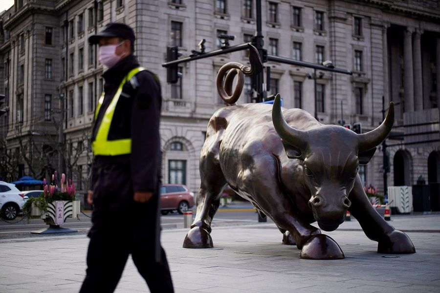 A security guard wearing a face mask walks past the Bund Financial Bull statue, on The Bund in Shanghai, China, on 18 March 2020. (Aly Song/File Photo/Reuters)