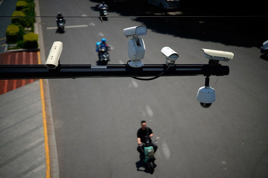 People ride scooters under surveillance cameras on a street in Shanghai, China, 9 May 2023. (Aly Song/Reuters)