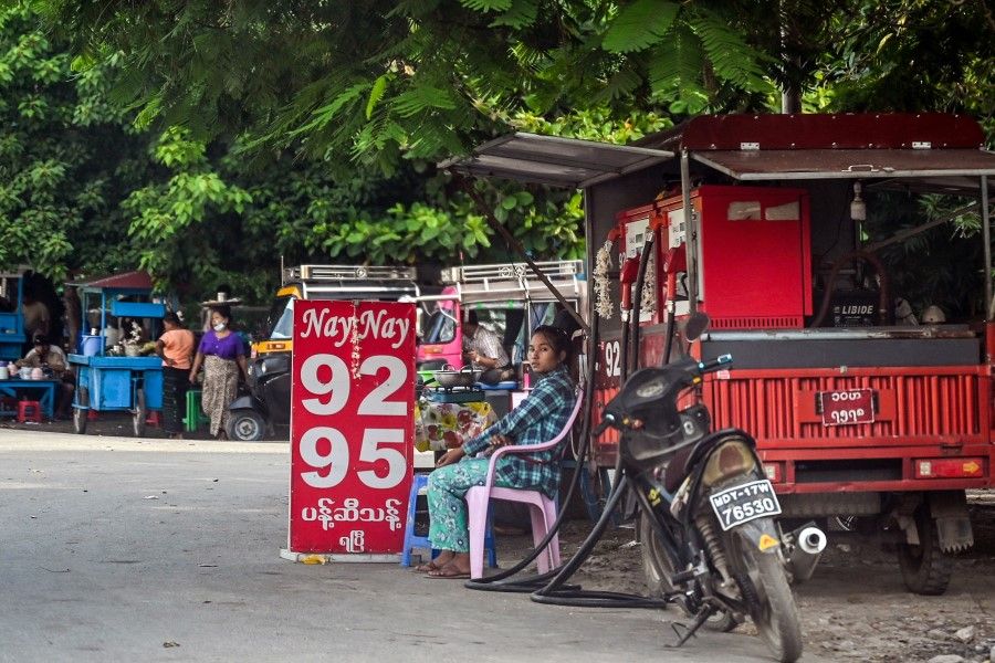This picture taken on 11 October 2021 shows a woman sitting next to her mobile gas station on a street in Mandalay. (STR/AFP)