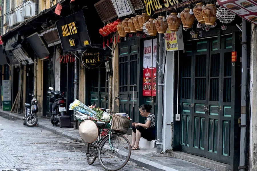 A street vendor sits near her bicycle carrying flowers to sell along a street in Hanoi on 24 July 2026.