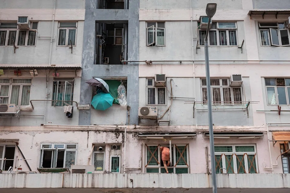 A woman (bottom C) climbs back into her apartment after taping the windows as Super Typhoon Ragasa moved towards Hong Kong on 23 September 2025. (Dale De La Rey/AFP)