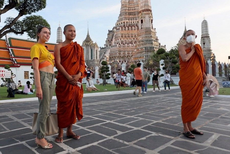 A screen grab shows a Western tourist posing for a picture with Buddhist monks during a city tour at Wat Arun temple in Bangkok, Thailand, 13 May 2023. (Jorge Silva/Reuters)
