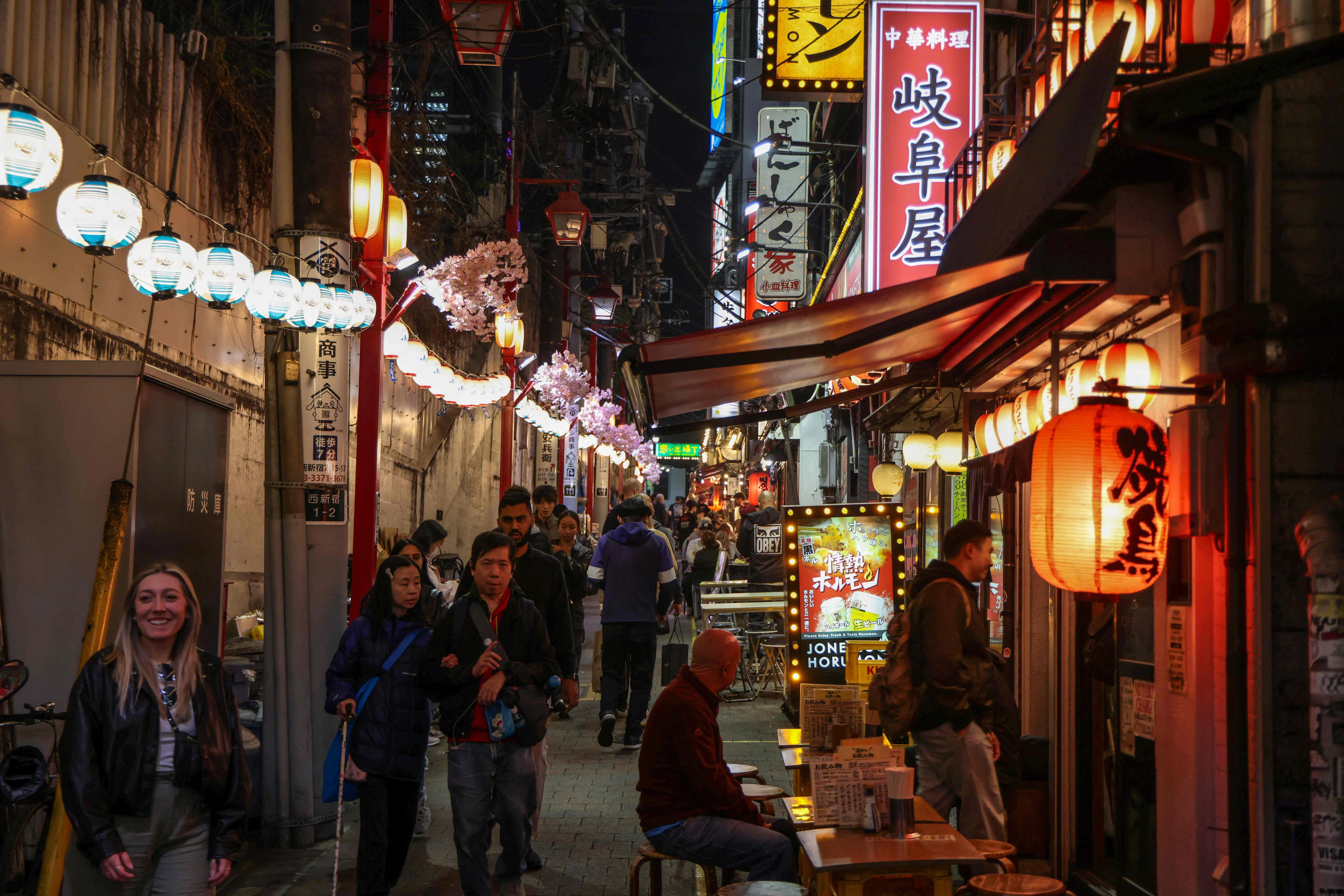 People walk past izakaya restaurants in the Shinjuku district in Tokyo on 30 March 2026.