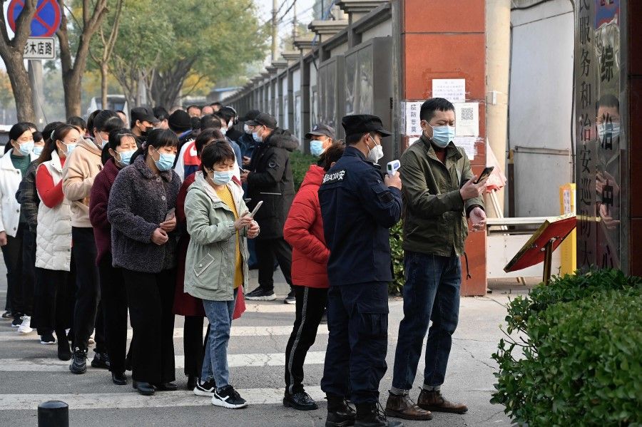 People wait in line to receive Covid-19 vaccination booster shots as a security guard checks body temperature of a man along a street in Beijing on 30 October 2021. (Jade Gao/AFP)