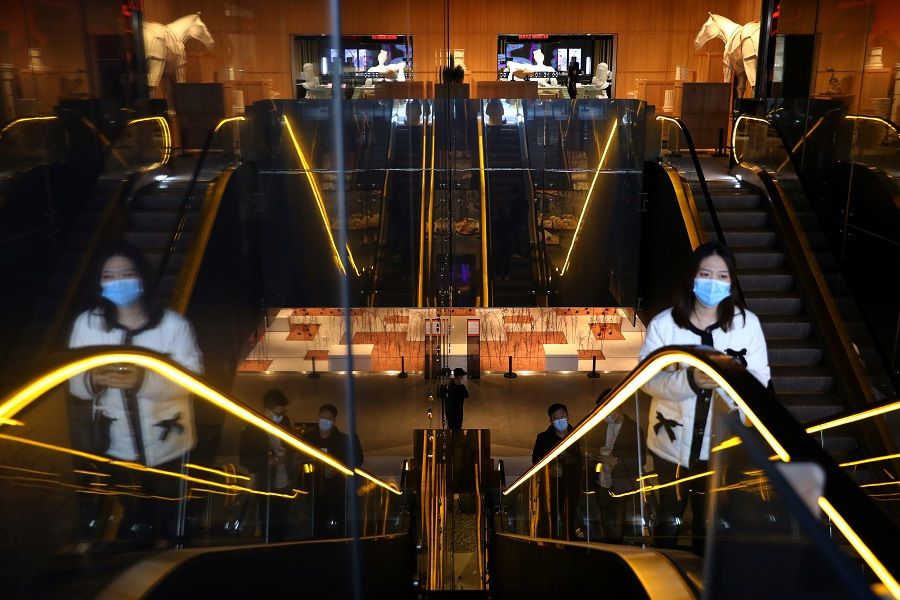 Customers wearing face masks ride on an escalator at a shopping mall in Beijing, China, 1 December 2021. (Tingshu Wang/Reuters)