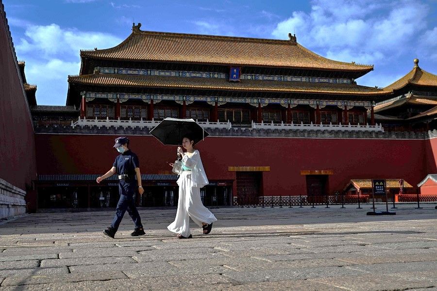 A woman protects herself from the sun with an umbrella while walking next to the entrance of the Forbidden City in Beijing, China on 7 June 2023. (Hector Retamal/AFP)