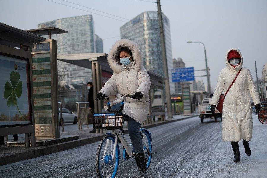 A woman wearing a face mask rides a bicycle on the street during a snowy morning in Beijing, China, 19 January 2021. (Carlos Garcia Rawlins/Reuters)