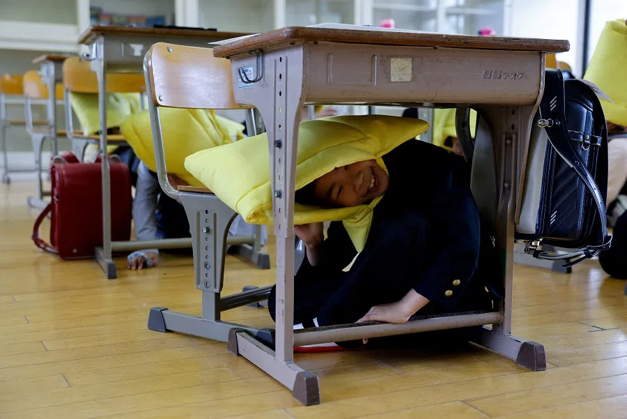 A tourist from China hides under the desk with disaster prevention hood during evacuation drill while taking part in a Japanese high school experience in Kimitsu, Chiba prefecture, Japan, on 23 April 2025. (Manami Yamada/Reuters)