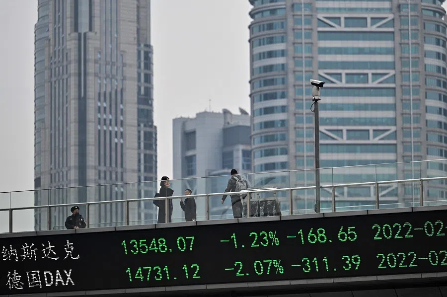 People walk across a bridge with a ticker board showing stock prices in the financial district of Shanghai, China, on 22 February 2022. (Hector Retamal/AFP)