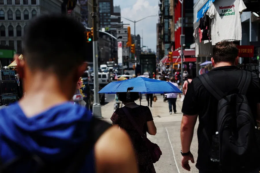 A woman walks with a parasol with others along Canal Street in the Chinatown area of New York City, US on 10 July 2024. 