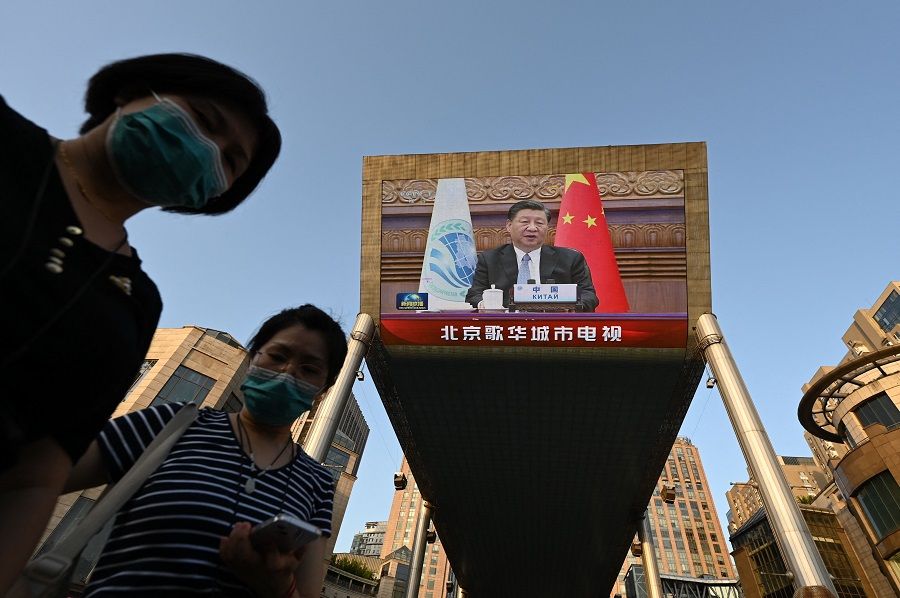 People are seen below a giant screen showing news footage of Chinese President Xi Jinping speaking virtually to the Shanghai Cooperation Organisation meeting, which was being held in India, at a shopping mall in Beijing, China, on 4 July 2023. (Greg Baker/AFP)
