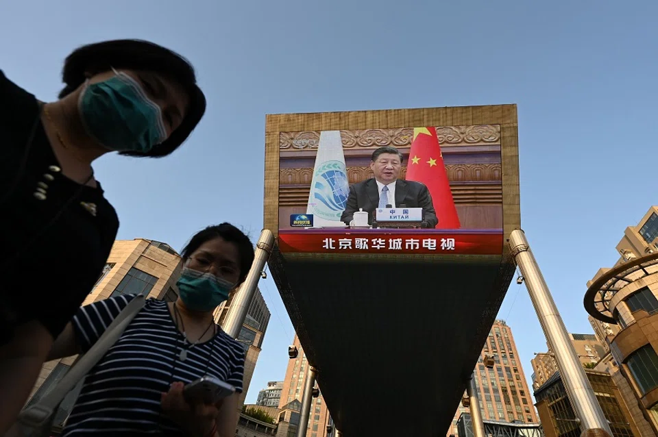 People are seen below a giant screen showing news footage of Chinese President Xi Jinping speaking virtually to the Shanghai Cooperation Organisation meeting, which was being held in India, at a shopping mall in Beijing, China, on 4 July 2023. (Greg Baker/AFP)