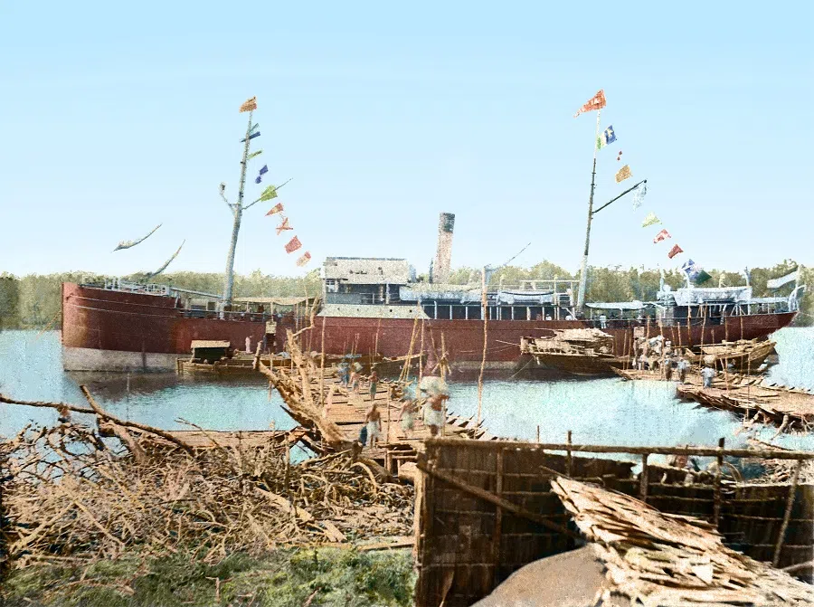 A Western cargo ship arriving at the Kallang River, 1900s. Workers have lined up small wooden boats to create two bridges between the pier and the ship, showing that the ship's capacity is quite large.
