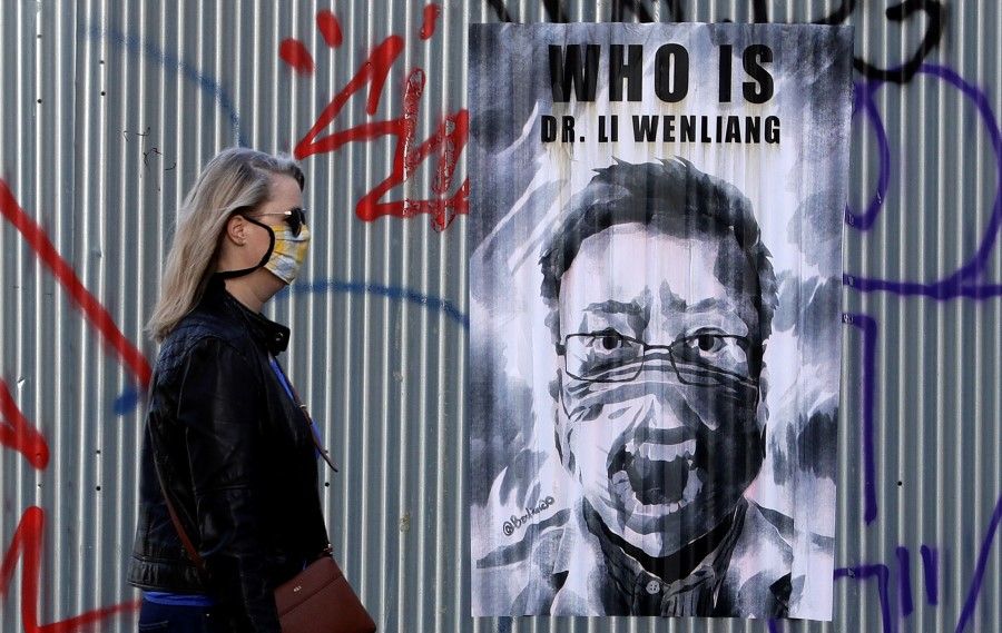 A woman in Prague walks past a poster of the late Li Wenliang, a Chinese ophthalmologist who tried to raise the alarm about COVID-19 and later died from it, March 27, 2020. (David W Cerny/REUTERS)