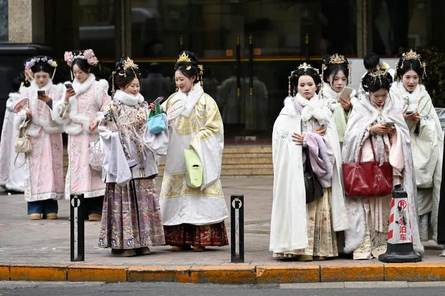 Women, dressed in traditional Chinese outfits, stand along a road in Beijing on 14 January 2026. (Wang Zhao/AFP)