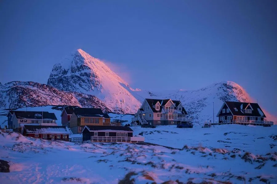 This photograph shows houses beneath snow covered mountains at dusk in Nuuk, Greenland, on 21 January 2026. (Jonathan Nackstrand/AFP)