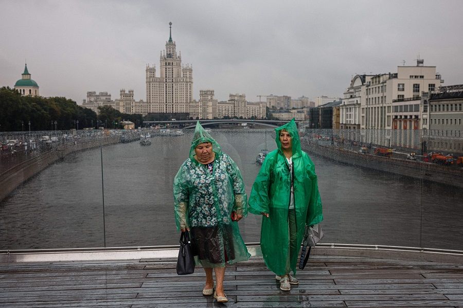 Women wearing plastic rain coats walk on a pedestrian bridge near a Stalin-era skyscraper on Kotelnicheskaya embankment on the northern bank of the Moskva River in Moscow, Russia on 11 August 2021. (Dimitar Dilkoff/AFP)