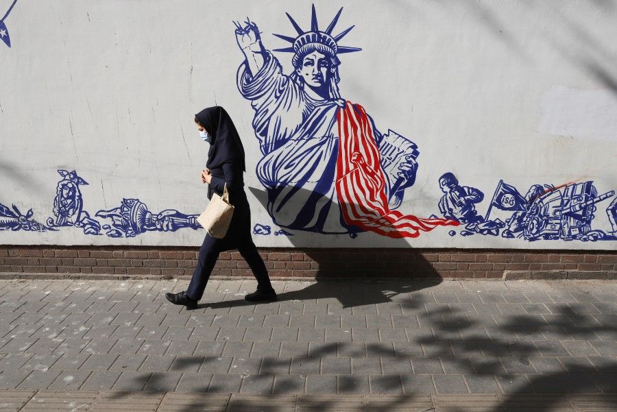 An Iranian woman wearing a face mask walks past a wall of the former US embassy with an anti-America mural on it in Tehran, Iran, 6 April 2021. (Majid Asgaripour/WANA (West Asia News Agency) via Reuters)