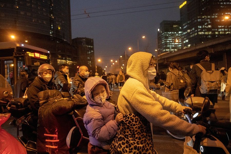 A woman and a child sit on a scooter as they wait in evening rush hour traffic in Beijing, China, 10 March 2023. (Thomas Peter/Reuters)