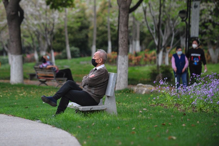 A man sits on a bench at a park in Wuhan, China, on 26 March 2020. (STR/AFP)