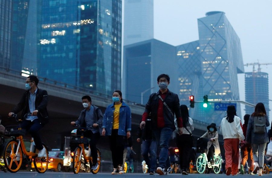 The skyline of the Beijing's Central Business District rises behind people crossing a street during evening rush hour, April 15, 2020. (Thomas Peter/REUTERS)