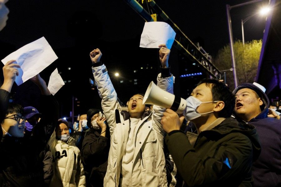 People shout slogans and hold up papers during a protest against Covid-19 restrictions after a vigil for the victims of a fire in Urumqi, in Beijing, China, 28 November 2022. (Thomas Peter/Reuters)