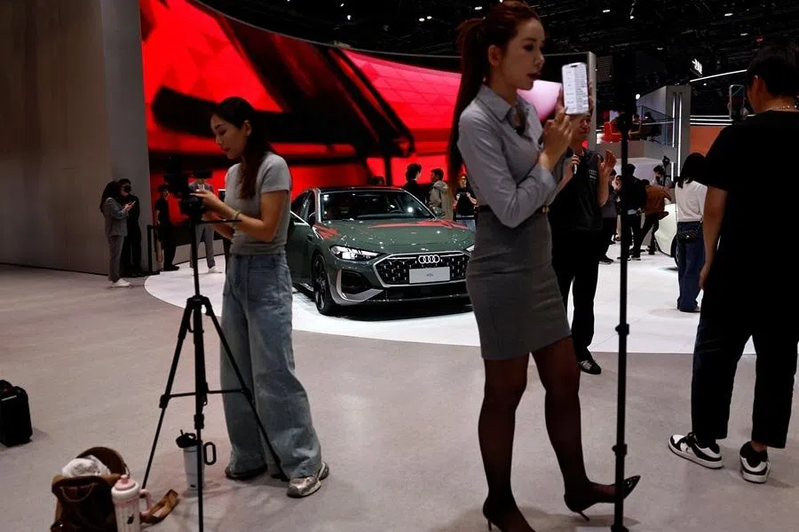 People work with their phones near an Audi A5L on display at the Beijing International Automotive Exhibition (Auto China), in Beijing, China, on 24 April 2026.