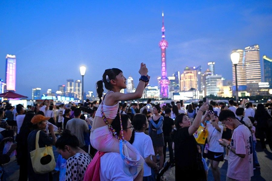 A child sitting on a man's shoulder takes a picture as she visits the Bund waterfront area in Shanghai, China, on 5 July 2023. (Wang Zhao/AFP)