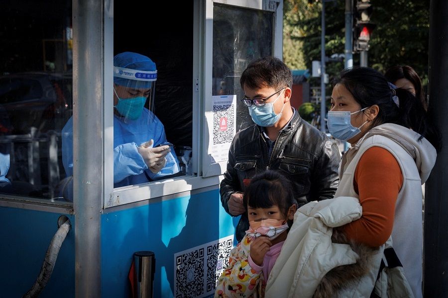 A pandemic prevention worker records personal details of people as they line up to get a swab test at a testing booth in Beijing, China, 3 November 2022. (Thomas Peter/Reuters)