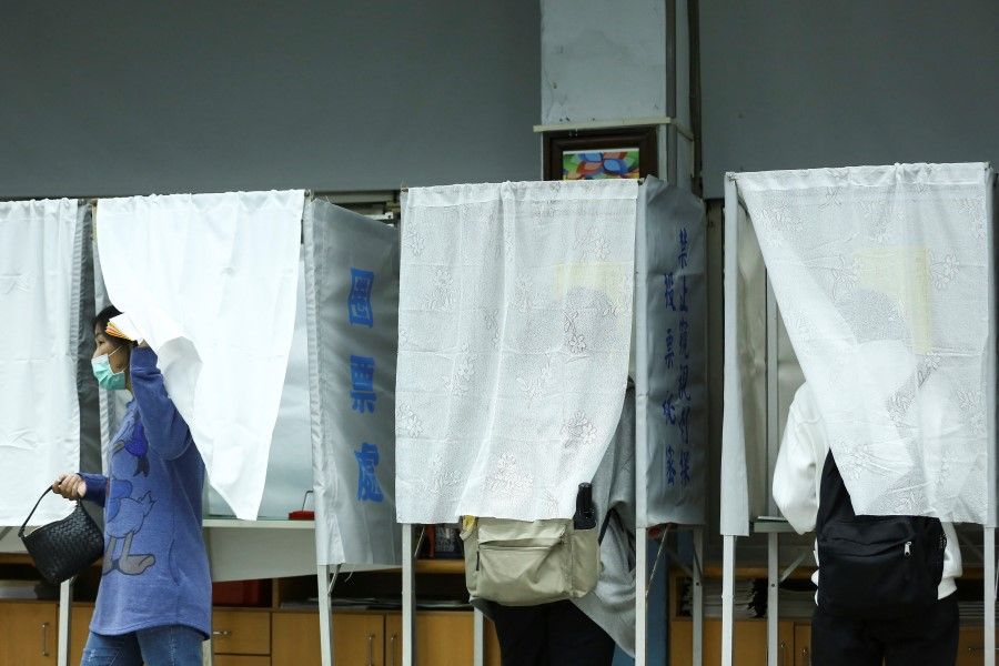 A woman wearing a face mask to prevent the spread of Covid-19, walks out from a booth at a polling station while participating in a four-question referendum in Taipei, Taiwan, 18 December 2021 (Annabelle Chih/Reuters)