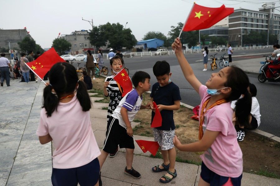 Children wave Chinese national flags on the street ahead of a rehearsal for the celebrations to mark the 100th founding anniversary of the Communist Party of China, in Beijing, China, 26 June 2021. (Tingshu Wang/Reuters)