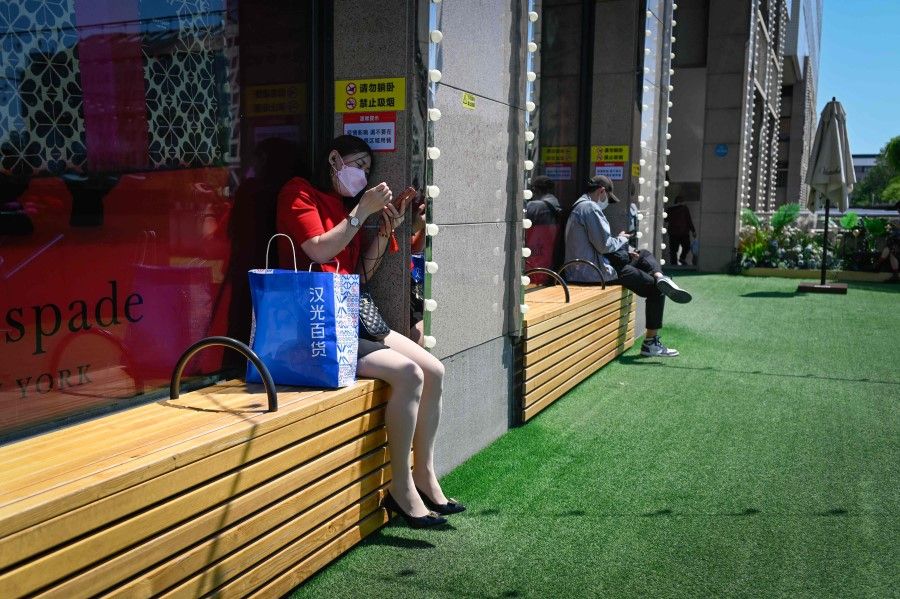 A woman uses her mobile phone as she rests on a bench outside a mall at a business district in Beijing on 16 May 2022. (Wang Zhao/AFP)