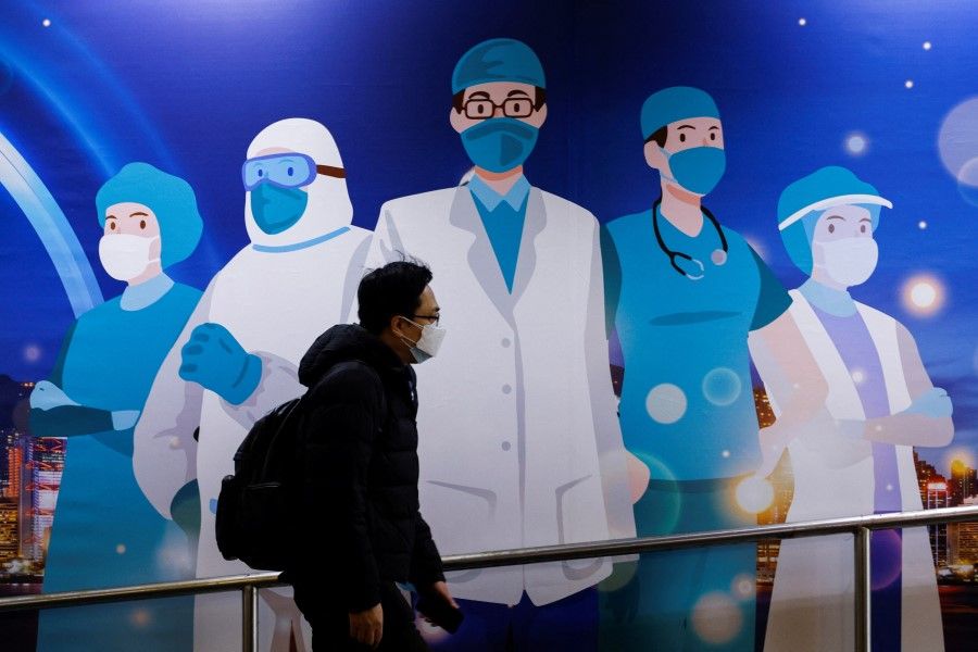 A man wearing a face mask walks past an advertisement to support medical professionals, following the Covid-19 outbreak, in Hong Kong, China, 24 February 2022. (Tyrone Siu/Reuters)