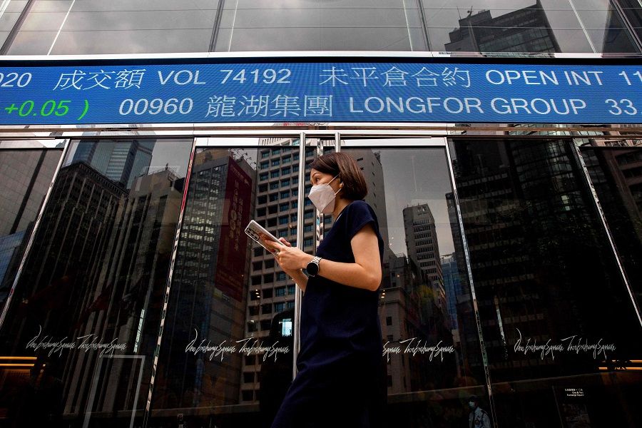 A woman walks past a digital sign showing stock market information in the Central district of Hong Kong on 5 November 2021. (Isaac Lawrence/AFP)