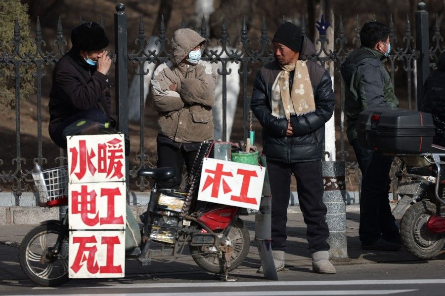 This photo taken on 1 March 2023 shows workers standing near signs advertising their skills as they wait on the street to be hired in Shenyang, in northeastern China's Liaoning province. (AFP)