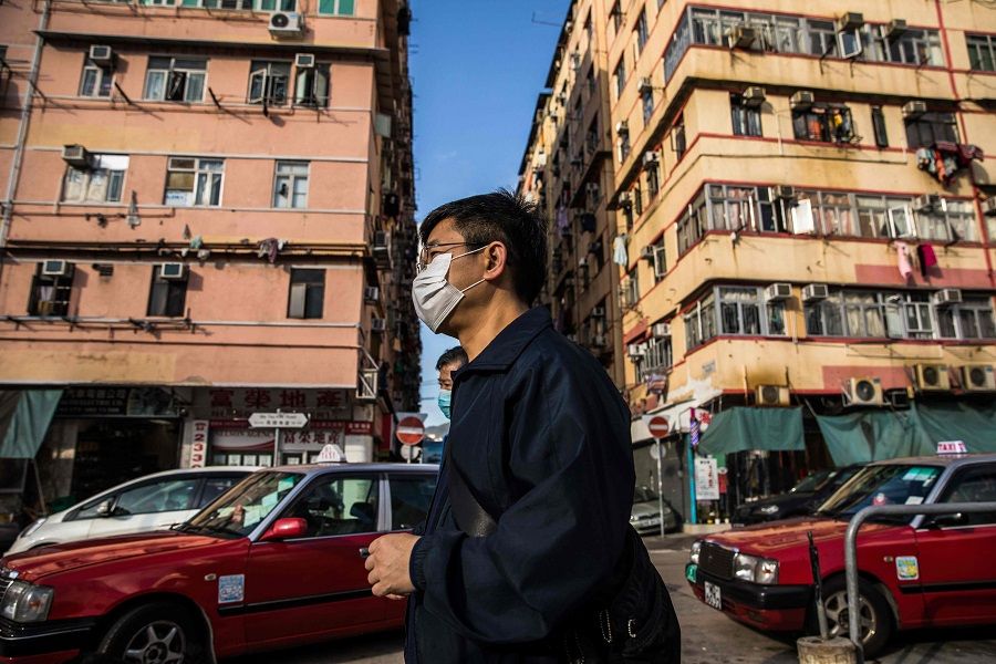 In this picture taken on 29 February 2020, people wearing face masks as a precautionary measure against the spread of the Covid-19 coronavirus walk past residential buildings in Hong Kong. (Dale De La Rey/AFP)