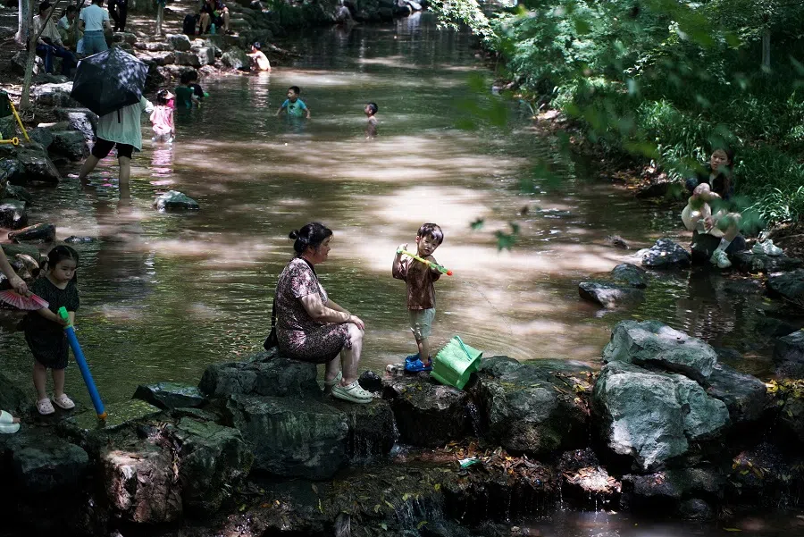People cool off in a stream at the Jiuxi, in Hangzhou, Zhejiang province, China on 2 August 2024. (Nicoco Chan/Reuters)