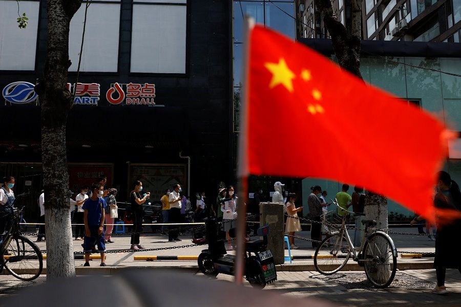 A Chinese flag flutters near people lining up to get tested at a makeshift nucleic acid testing site, amid Covid-19 outbreak in Beijing, China, 18 May 2022. (Carlos Garcia Rawlins/Reuters)