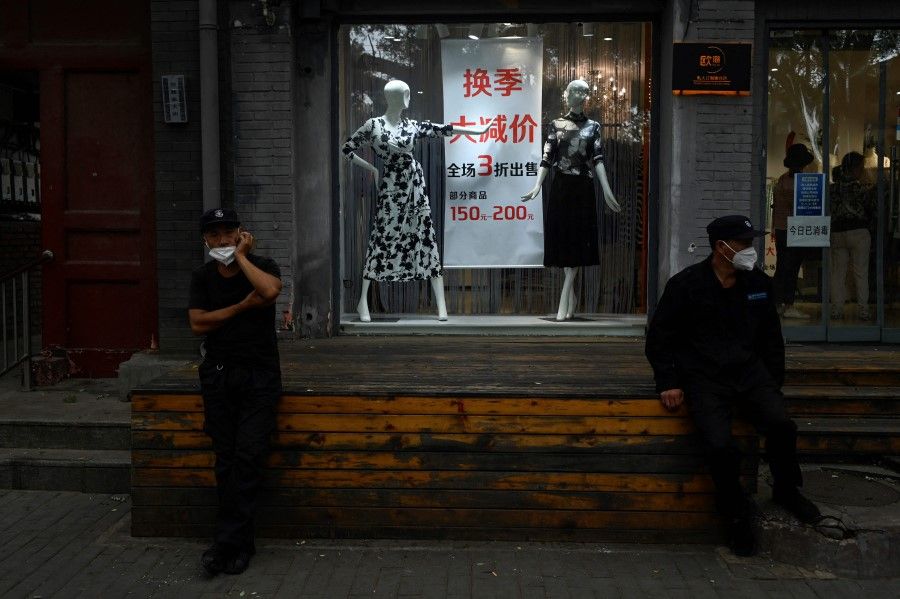 Two security guards sit at the entrance of a shop in Beijing on 29 August 2022. (Wang Zhao/AFP)