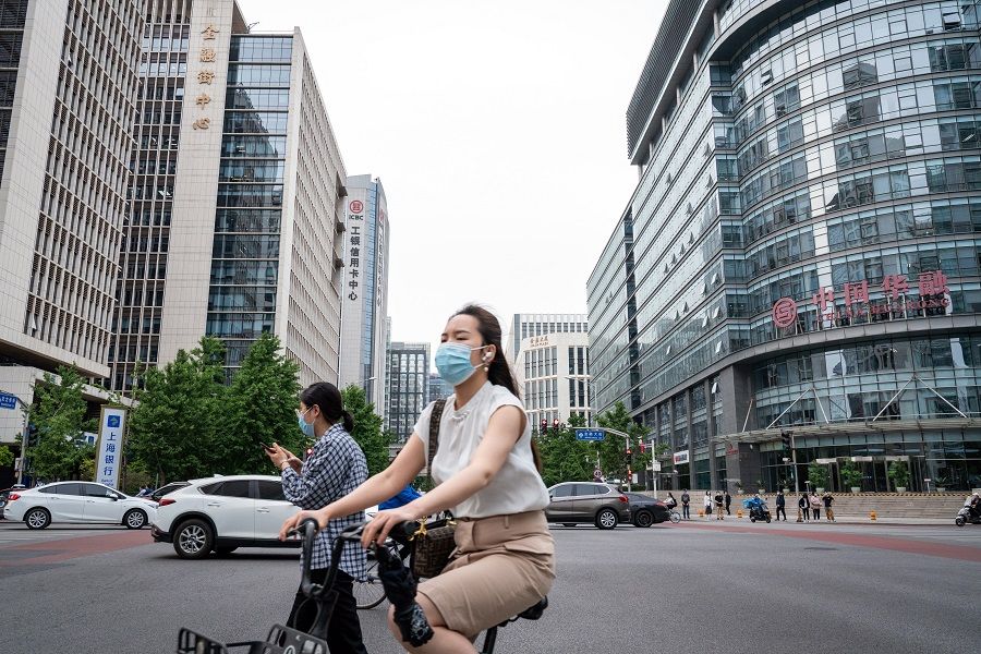 A cyclist and pedestrians wearing protective masks travel past buildings on Financial Street in Beijing, China on 19 May 2021. (Yan Cong/Bloomberg)