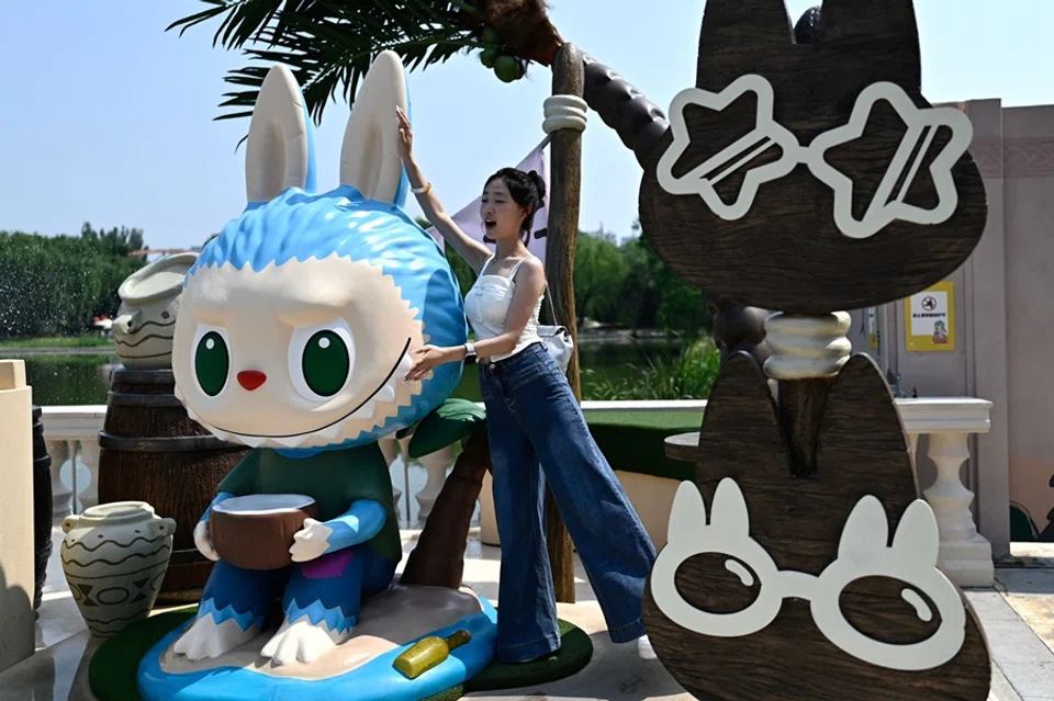 This picture taken on 18 June 2025 shows a woman posing for a picture next to the character Labubu as she visits Pop Mart’s theme park Pop Land in Beijing, China. (Pedro Pardo/AFP)