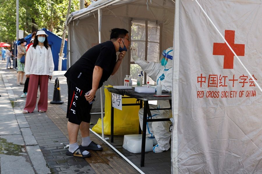 A medical worker in a protective suit collects a swab from a resident at a makeshift PCR testing site amid the Covid-19 outbreak in Beijing, China, 25 May 2022. (Carlos Garcia Rawlins/Reuters)