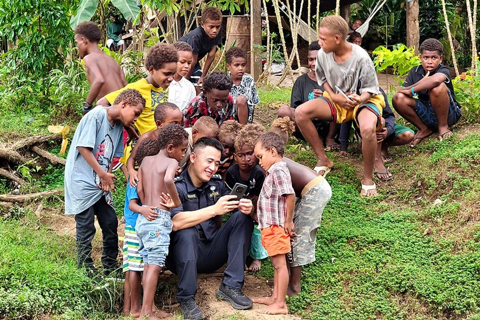 In this undated photo released by the Royal Solomon Islands Police Force and received by AFP on 20 June 2025, a member of the Chinese Police Liaison Team is surrounded by children as he holds a phone during a ‘community engagement event’ in the capital of Honiara, in the Pacific nation of Solomon Islands. (Handout/Royal Solomon Islands Police Force/AFP)