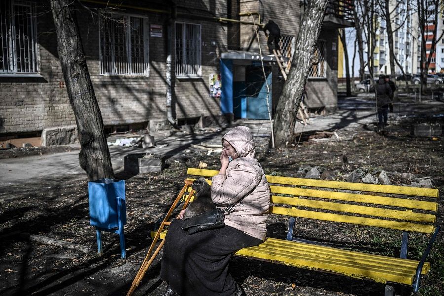 A woman weeps as she sits outside a building that was damaged by bombing in the eastern Ukraine town of Kharkiv on 24 February 2022. (Aris Messinis/AFP)