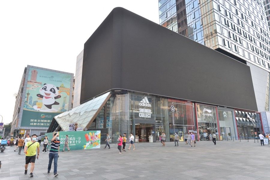 This photo taken on 17 August 2022 shows people walking past a screen which is shut down to save energy in Chengdu, in China's southwestern Sichuan province. (AFP)
