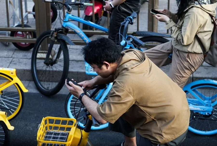 People on bicycles use smartphones as they wait for a green light at a junction, in Beijing, China, on 19 May 2026.