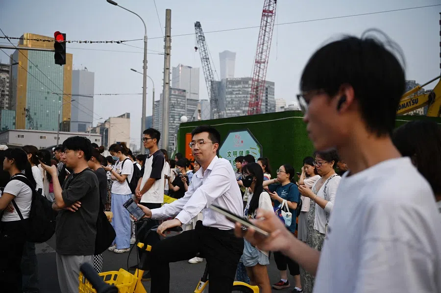 People wait to cross a road near a construction site in Beijing, China on 9 July 2024. (Greg Baker/AFP)