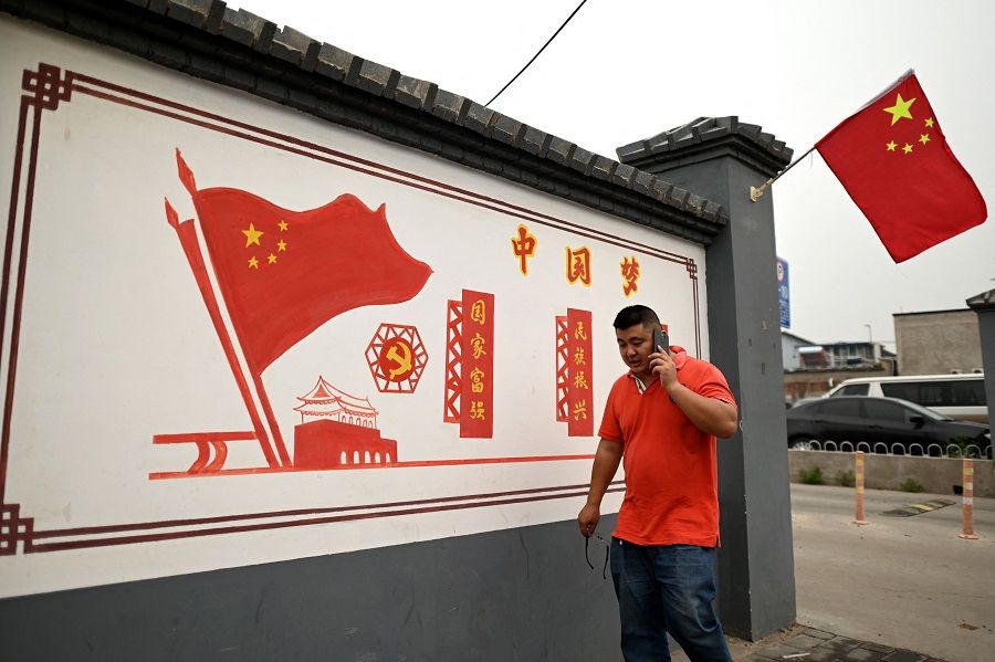 This photo taken on 9 June 2021 shows a man walking past a propaganda mural that reads "Chinese Dream: Make the country prosperous and strong, rejuvenate the nation" along a street in Beijing, China. (Noel Celis/AFP)